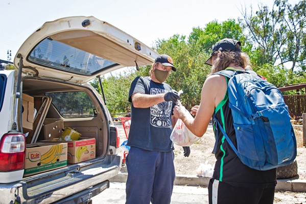 A HELPING HAND Paul Andreano, a volunteer with Hope's Village of SLO, hands out food to people living near the Bob Jones Trail. - PHOTO BY JAYSON MELLOM