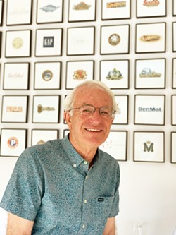 DECADES OF DESIGN Pierre Rademaker stands in front of a wall of his graphic design creations. - PHOTO BY MALEA MARTIN