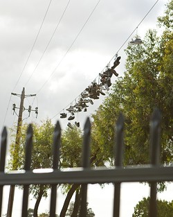 'SHOEFITI':  Architecture major Bradley Williams expounds on how a collection of shoes hanging from the telephone wires over a common shortcut for students was elevated to &ldquo;public art.&rdquo; When the city created a fence to block off the footpath, the shoe sculpture changed from an evolving part of the landscape to a cordoned-off curiosity. - PHOTO BY STEVE E. MILLER