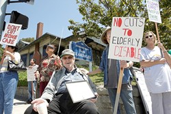 NOT WITHOUT A FIGHT :  If state budget cuts go through, 71-year-old Dale Grube (center, seated) worries he&rsquo;ll lose the freedom of his apartment, because without his caretaker he&rsquo;ll be forced to live in a convalescent home. - PHOTO BY STEVE E. MILLER