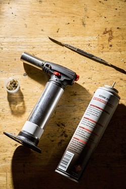 AN EXPLOSIVE TREND:  All the makings for smoking concentrated cannabis (minus the bong), and a can of butane. Using specialized implements that attach to bongs, a metal piece is heating with a torch, and then a dab is placed on the metal, causing it to burn. - PHOTO BY HENRY BRUINGTON
