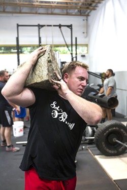 FUNCTIONAL FITNESS SLO Strong co-founder Andrew Wickham carries a large rock at a team workout in June at Headstrong Fit in SLO. - PHOTO BY JAYSON MELLOM