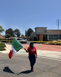 RALLYING FOR CHANGE Protest organizer Andrea Uvias waves the Mexican flag in front of the Santa Maria ICE office, where police put up yellow caution tape.
